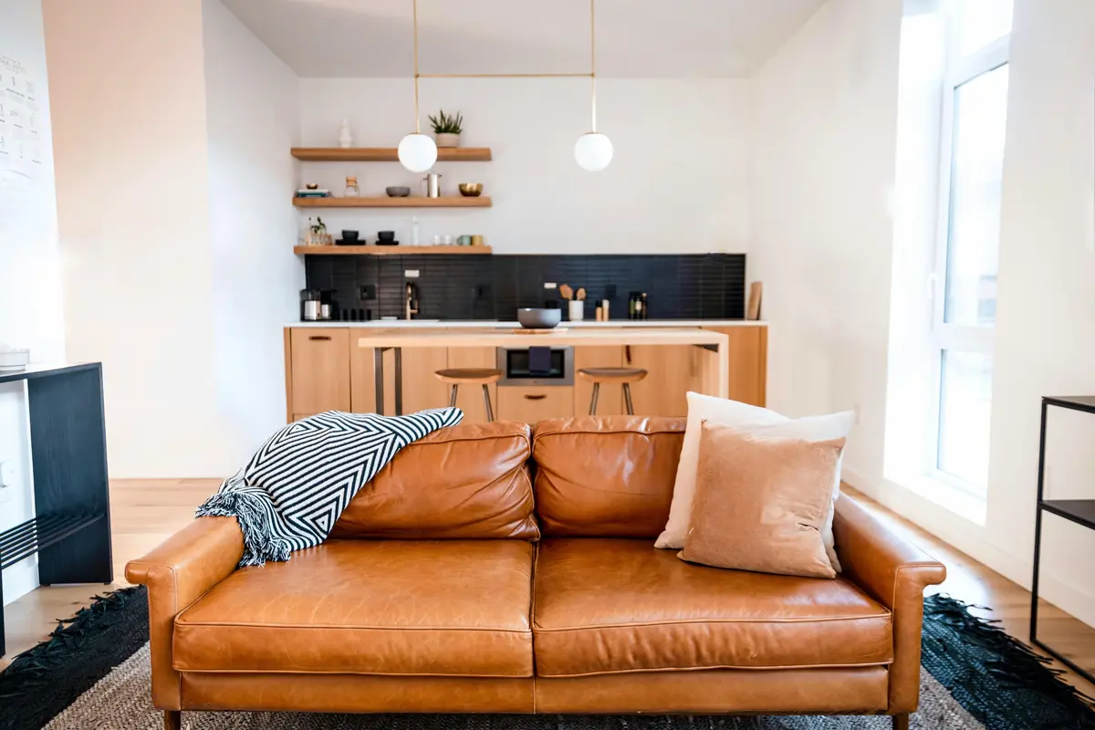 Інтер'єр сучасної однокімнатної квартири-студії: шкіряний диван рудого кольору на передньому плані та компактна зона кухні з островом на фоні.